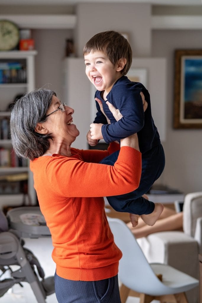 Happy smiling grandmother playing with her little grandson holding him in her arms in the air