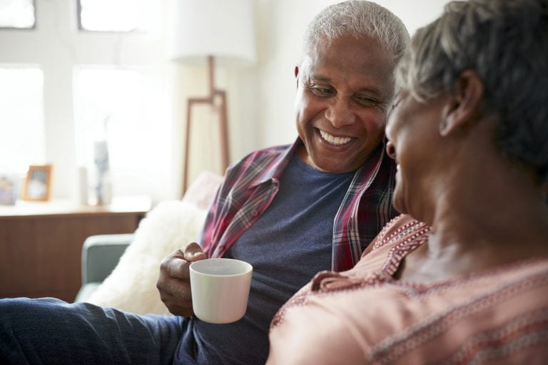 Senior Couple Sitting On Sofa At Home Relaxing With Hot Drink
